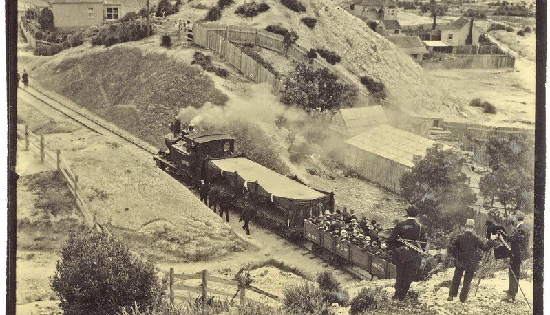 An old black and white photo of a train travelling through the hills of the West Coast.