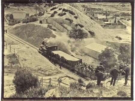An old black and white photo of a train travelling through the hills of the West Coast.