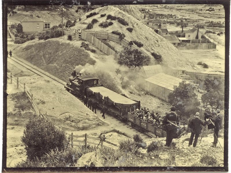An old black and white photo of a train travelling through the hills of the West Coast.