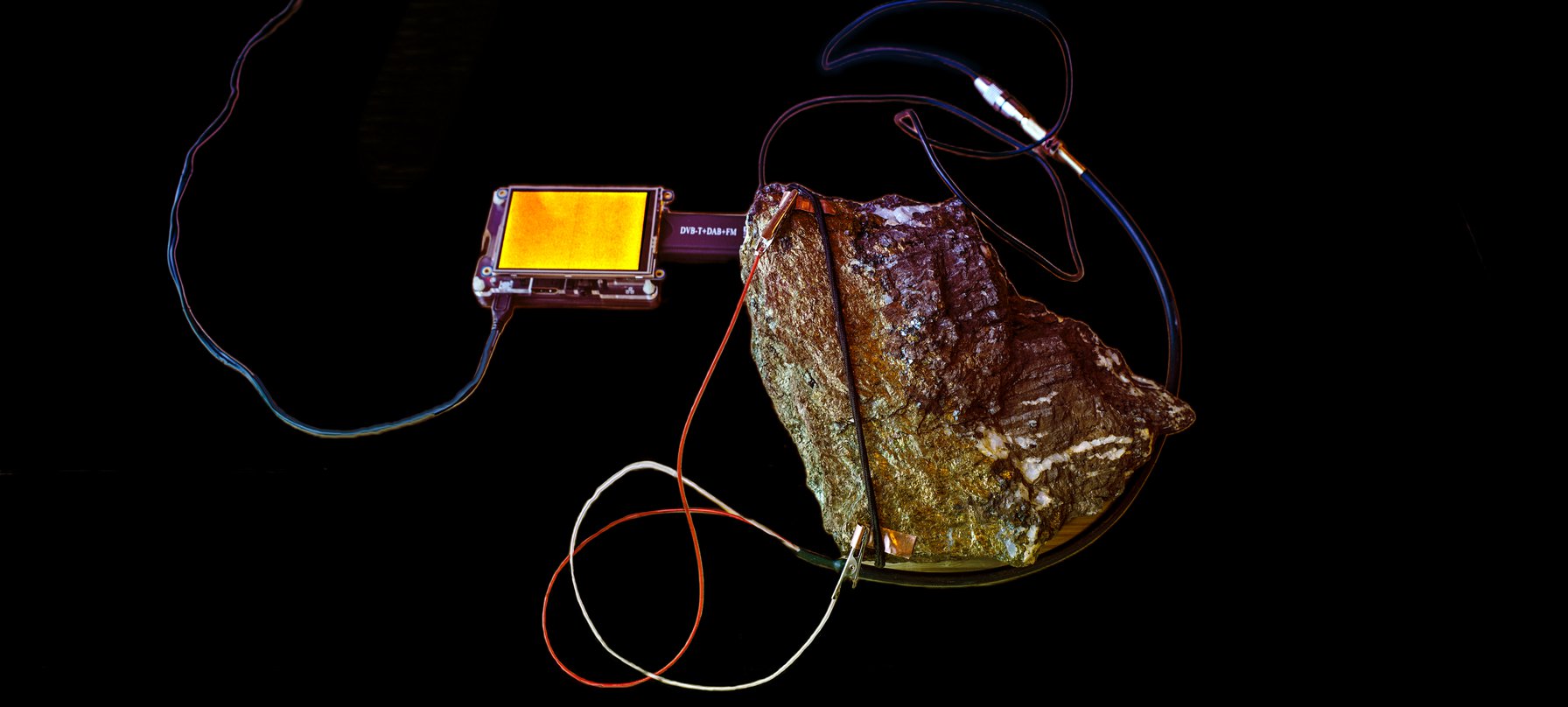 Ore-ic Radios and The Queen River Battery image. A photo of a rock covered in wires connecting it to a radio. Credit Haines and Hinterding.