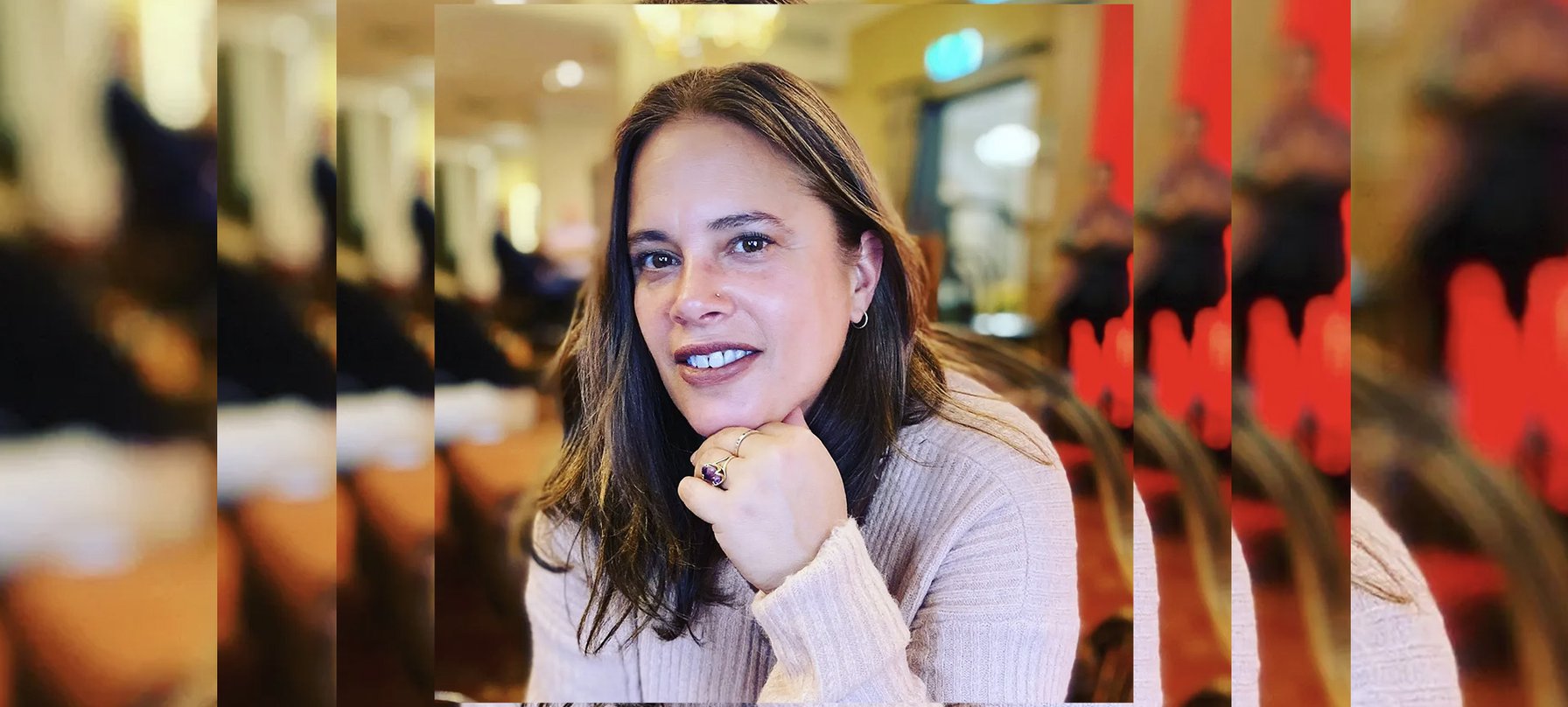 A photo of Yvania Bartholomeusz looking at the camera with her head propped up on her hand. On Yvania's finder is a ring with intricate curling gold metal and a shining purple stone in the centre. Credit Yvania Bartholomeusz.