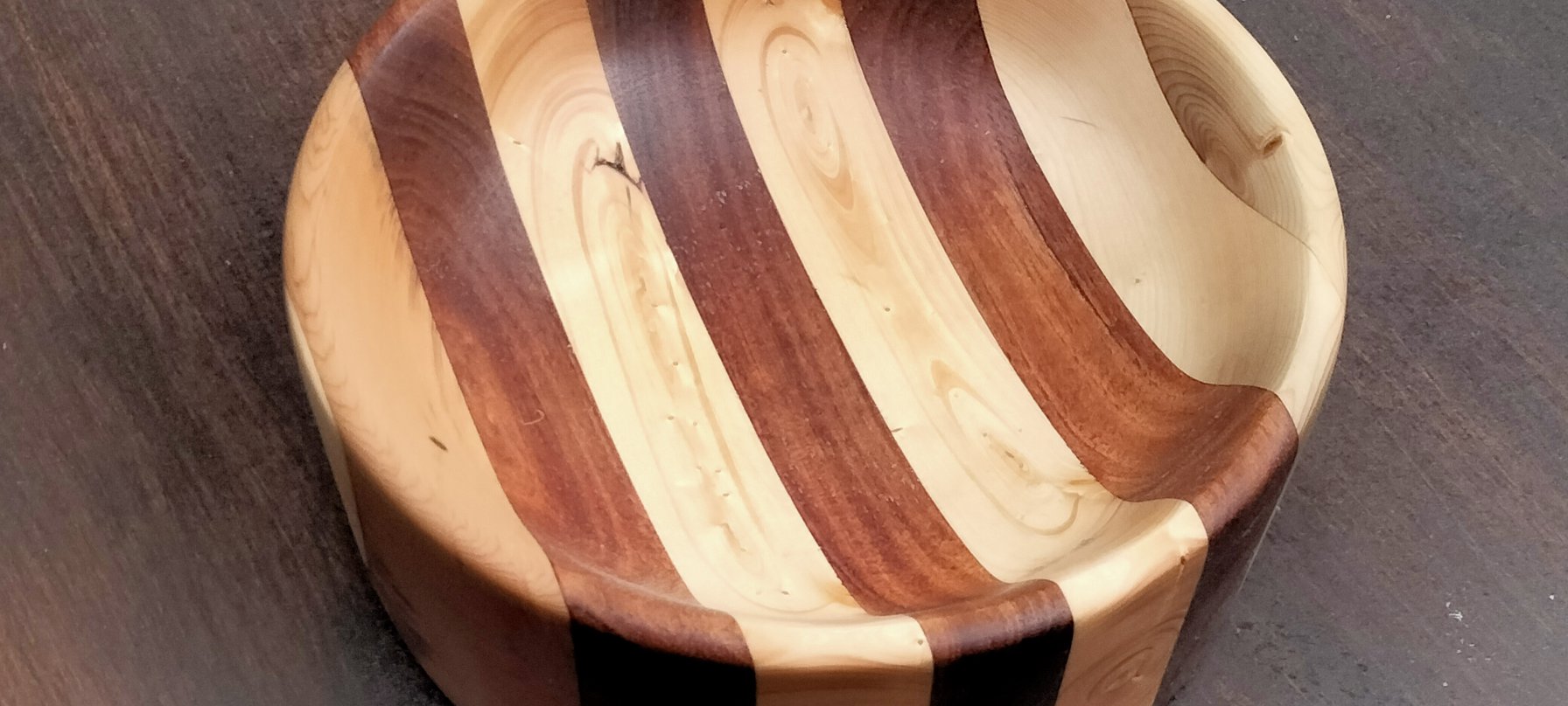 A photo of a smooth wooden bowl with alternating grains of light and deep brown wood running through its entirely. The bowl is sanded and oiled to look smooth and silky. Image West Coast Connect Inc.