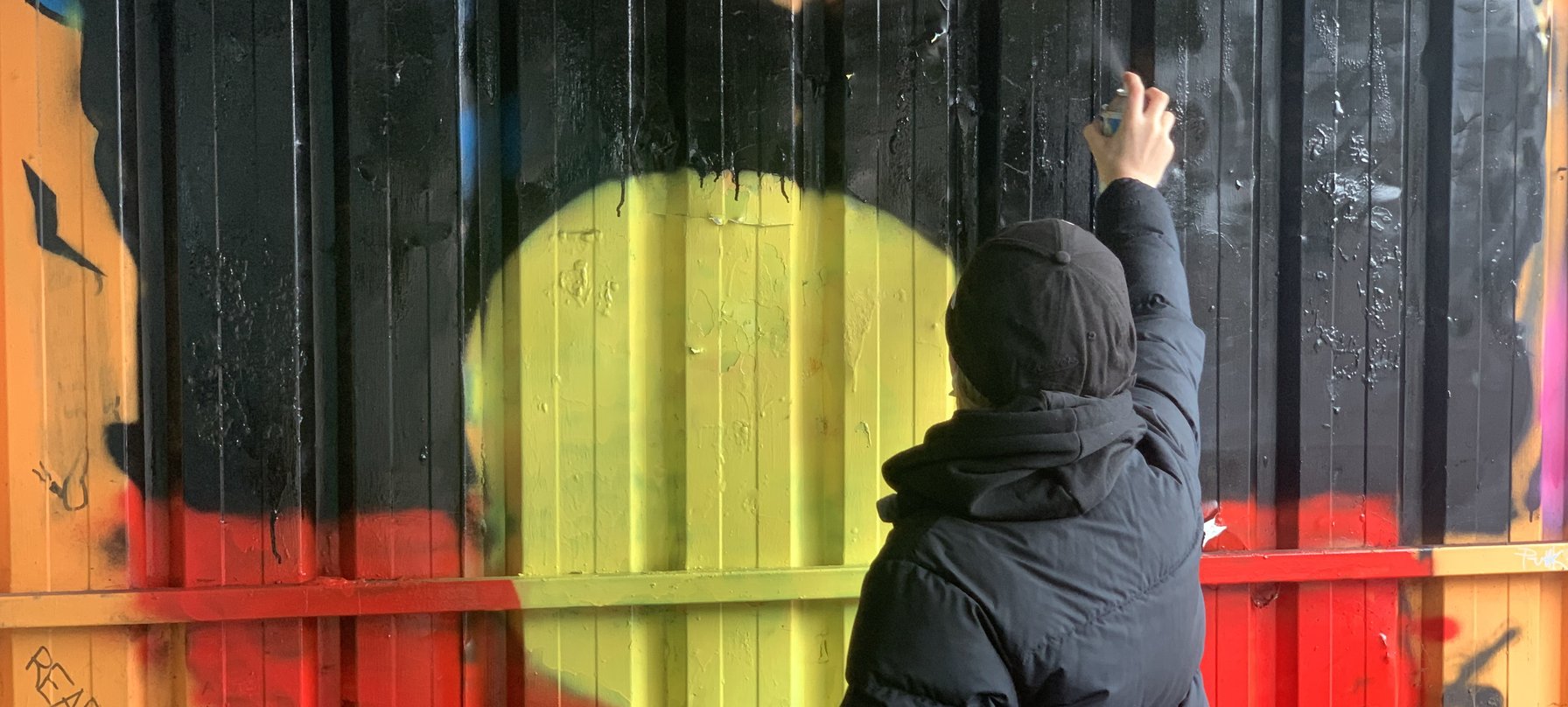 A photo of a person spray painting an artwork of an aboriginal flag.