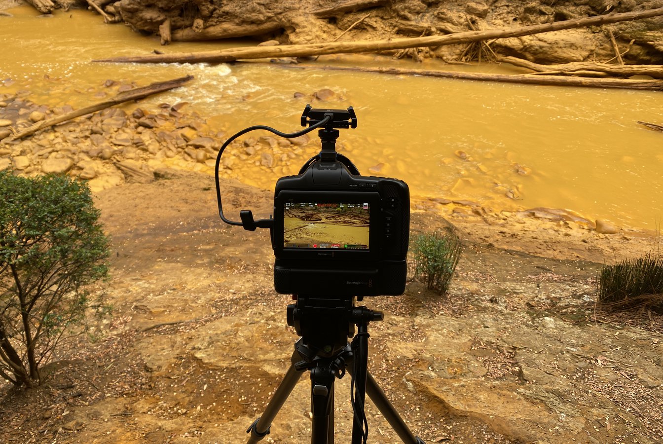 A photo of a camera on a tripod on the banks of an orange river, documenting the scene. Photo courtesy of Polly Stanton.