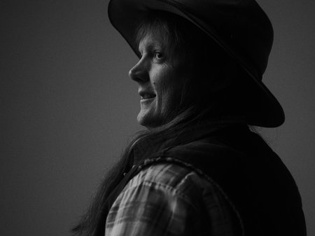 Artist Watty Thompson stands side-on in a black-and-white photograph, wearing a fedora and smiling softly.