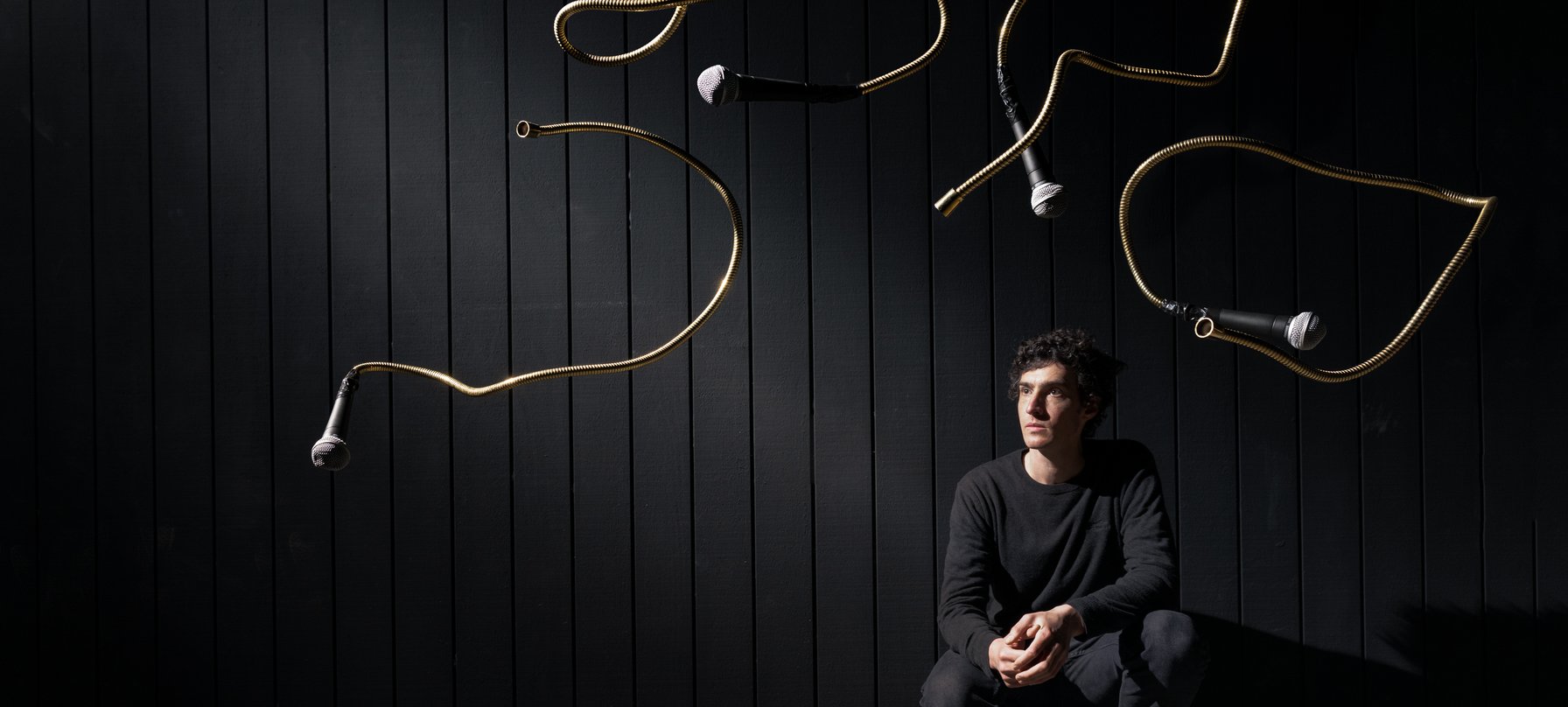 Microphones suspended in the air as artist Dylan Sheridan crouches on one knee