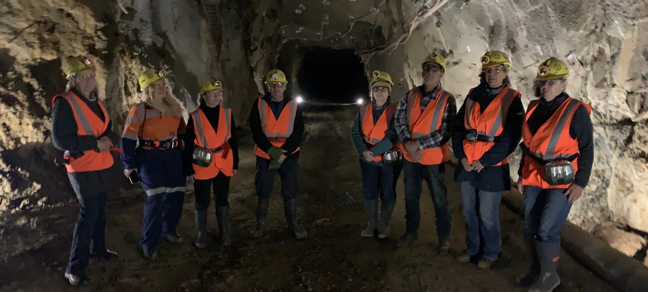 A photo of the Queenie Quoir in the Mount Lyell Underground Mine. 8 choir members are dressed in yellow hard hats with headlamps, and orange high visibility vests. Credit Polly Stanton.