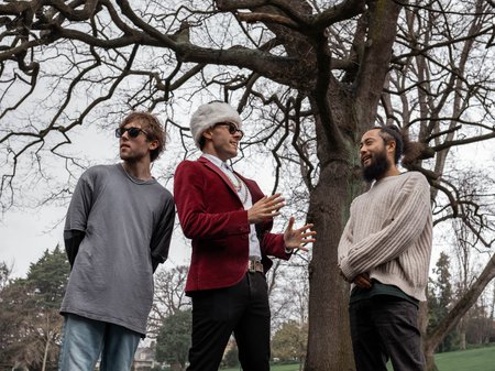 A photo of the 3 Slaughterhäus Surf Cult band members. 2 people wear sunglasses. 1 wears a fluffy hat and a gold chain. The background is a tall tree with no leaves. Credit Mell Schmeider.