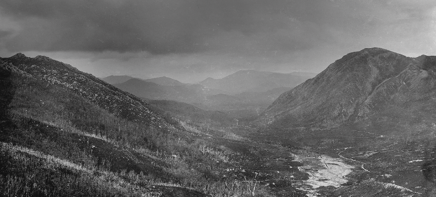 In the Footsteps of Charles Gould image. A black and white photo of zig-zagging tracks down the face of a mountain leading to wetlands at the base. Credit Beattie Hobart, Tasmanian Archive and Heritage Office.