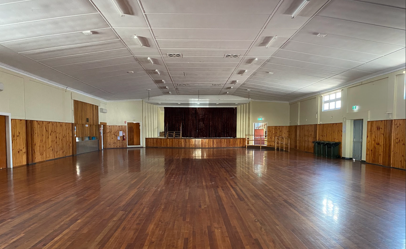 A photo inside the Queenstown Memorial Hall space. The flooring is varnished wood and there is a stage a t one end of the room.