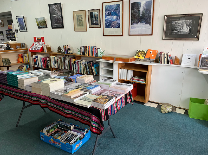 A photo taken from the entryway of Missing Tiger Bookshop, Queenstown. Bookshelves filled with books line the walls and a table full of books sits in the center of the space.