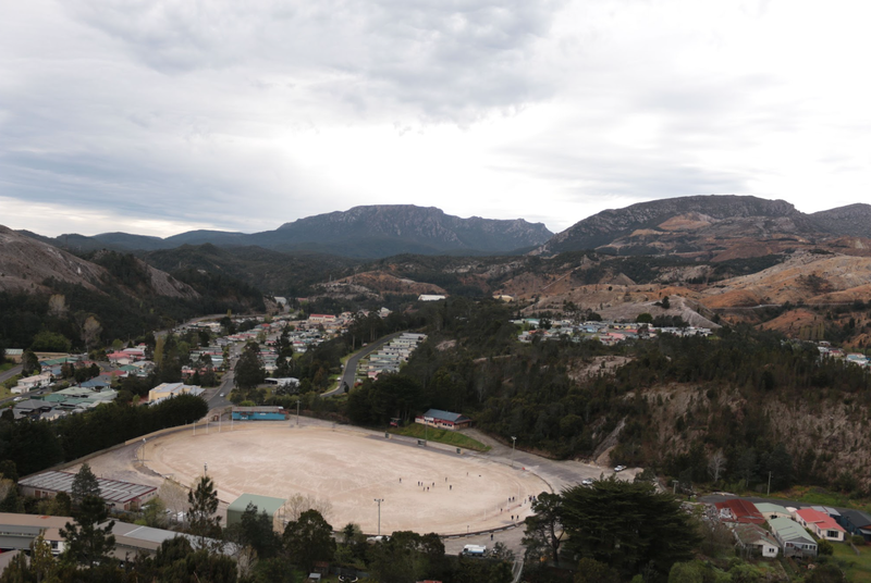 A photo of Queenstown Football Ground taken from on top of a hill. The photo shows the gravel oval in its entirety.