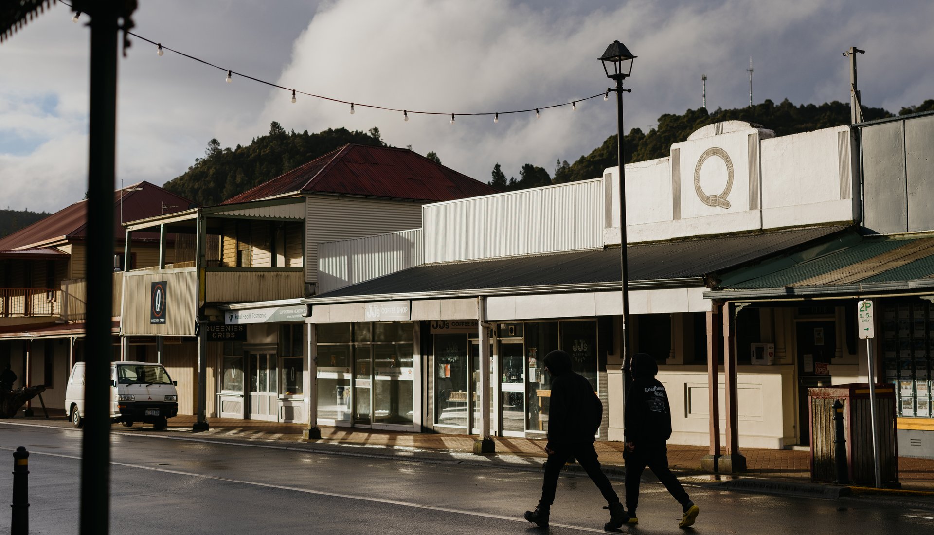 A photo of Queenstown's main street with two people walking past the Queenstown Club. Credit Jesse Hunniford