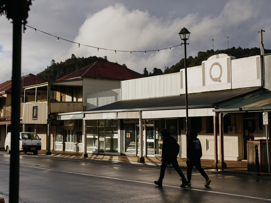 A photo of Queenstown's main street with two people walking past the Queenstown Club. Credit Jesse Hunniford