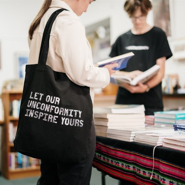 Image of person carrying a The Unconformity tote bag and reading a book in a bookshop.