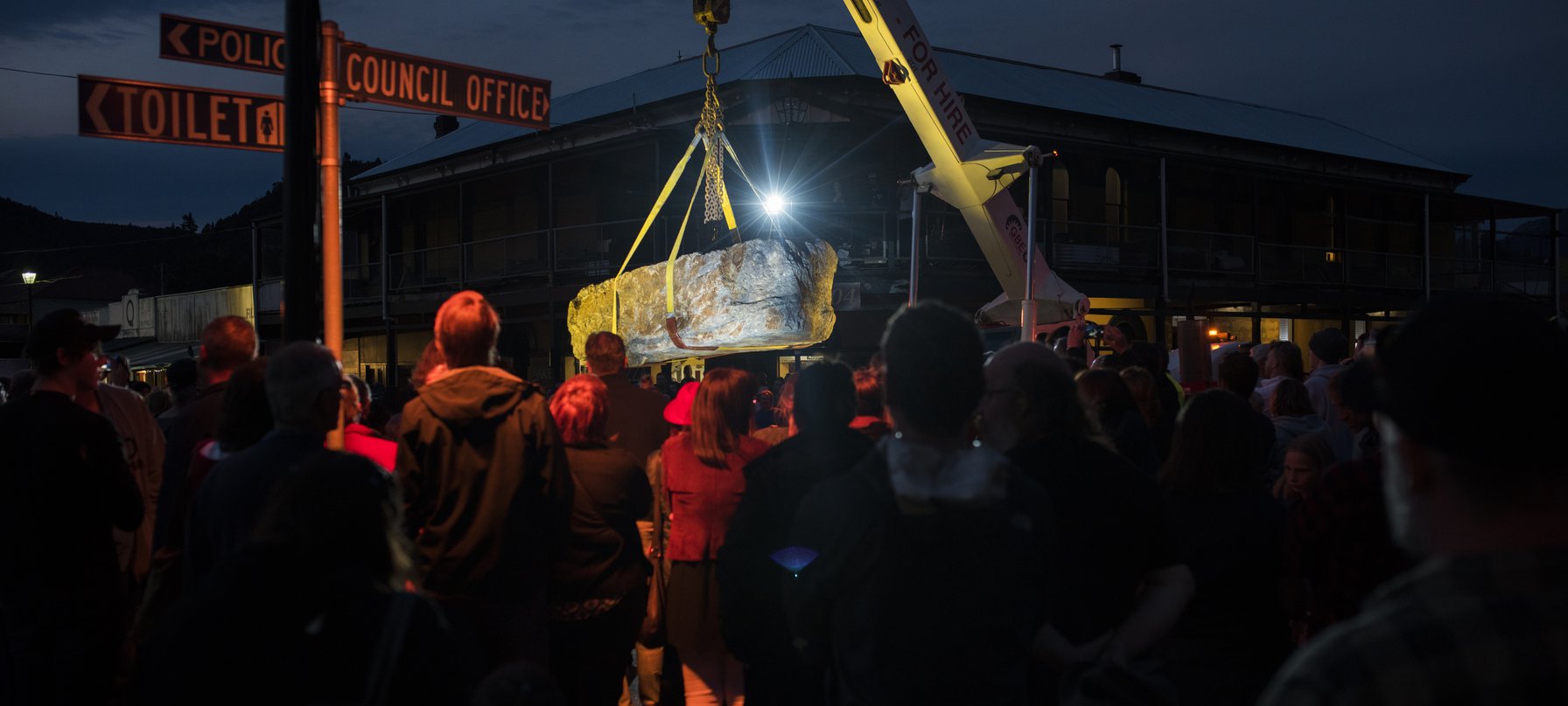 A photo of an audience surrounding a crane holding up a large stone, taken at The Unconformity 2018