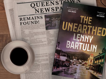 A photo of 'The Unearthed' novel by Lenny Bartulin laying on top off a newspaper, beside a cup of black coffee.