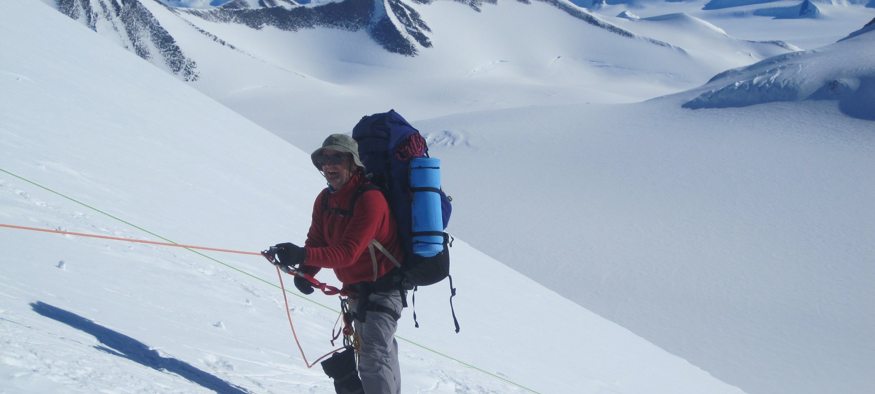 A photo of John Carswell, dressed in cold weather hiking gear, holding onto a rope as he ascends a snowy mountain range. Image courtesy of John Carswell.