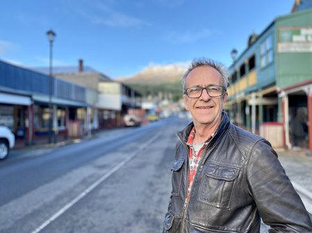 A photo of David "Fitzy" Fitzpatrick standing on Orr Street, Queenstown. Fitzy is smiling and wearing a flannelette shift under a leather jacket.