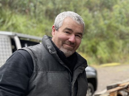 Michael Schlitz stands in front of his ute, with a dense dark green forest behind him and timber scattered across the ground.
