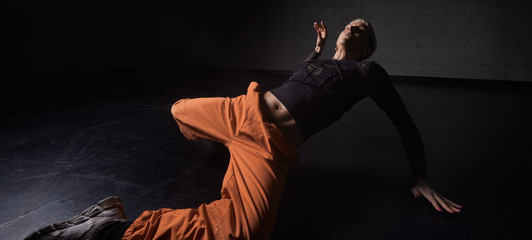 A photo of Jenni large sweeping her body onto the floor. Jenni's head and right arm stay high as their leg's extend onto the floor. Credit Pedro Greig.