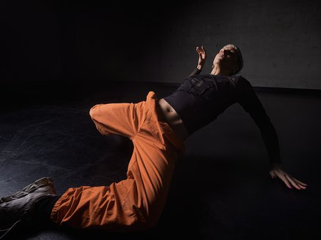 A photo of Jenni large sweeping her body onto the floor. Jenni's head and right arm stay high as their leg's extend onto the floor. Credit Pedro Greig.