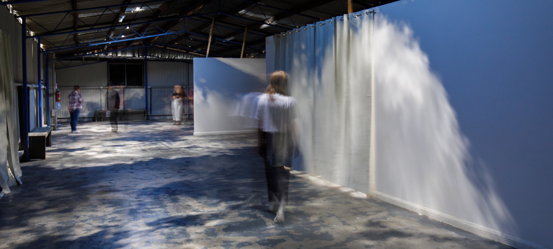 A photo of Priscilla Beck's work, 'fragile things.' A person walks through a gallery space with Pricilla's work projecting sky and clouds all around them. Credit Jesse Hunniford.